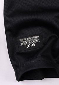 Μαύρο αθλητικό ύφασμα με υφασμένη επιφάνεια· διαθέτει ετικέτα ρούχου με λευκό κείμενο που γράφει "ACTIVE DISCOVERY" και λογότυπα.