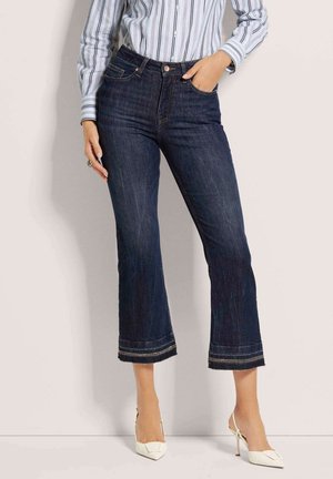 Donkerdenim cropped jeans met een rechte pasvorm, voorzien van een onafgewerkte zoom en contrasterende stiksels, gecombineerd met witte high heels.