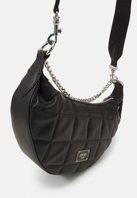 Borsa a tracolla nera trapuntata con una silhouette arrotondata, caratterizzata da un accento a catena e una tracolla in tessuto. Placca con logo metallico visibile sul davanti.