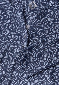 Marineblauwe stof met een golvende witte patroon, voorzien van een kraag en twee zichtbare knopen. Zachte textuur.