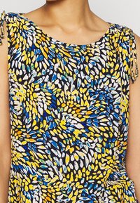 Blusa sin mangas con estampado floral en negro, que presenta acentos en amarillo, azul y blanco. Tiras ajustables en los hombros, textura de tela suave.