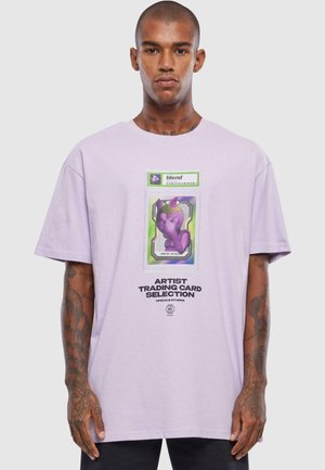 Lavendel bomull t-skjorte med løs passform, med et livlig grafikk av et karakterkort og fet tekst i midten.