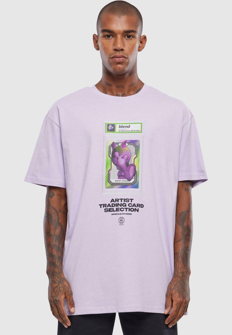 Lavendel-cotton t-shirt med løs pasform, der har et livligt grafisk motiv af et karakterkort og fed tekst i midten.