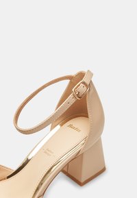 Beige högklackad sko med en fyrkantig akrylklack, överdel i läder, justerbart ankleband med en guldfärgad spänne och glänsande innersula med varumärkeslogotyp.