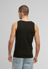 Black sleeveless tank top made of cotton, featuring a round neckline and a fitted design. The fabric has a smooth texture.
