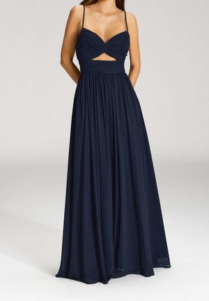Femme portant une robe bleu marine sans manches avec de fines bretelles et un corsage froncé avec une petite ouverture sous la poitrine.
