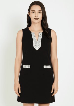 Vestido negro sin mangas con un escote decorativo de encaje blanco y dos bolsillos con acentos perlados. Textura suave y diseño ajustado.
