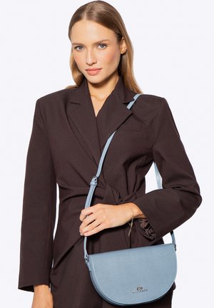 Hellblaue Leder-Umhängetasche mit glatter Oberfläche, halbkreisförmiger Form und einfachem Verschluss. Verfügt über einen dünnen, verstellbaren Riemen und ein Logodetail.