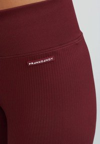 Bordeaux ribgebreide legging met een gladde textuur, voorzien van een wit merklabel op de tailleband.