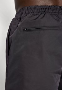 Black athletic shorts with an elastic waistband, side pockets, and a secure zippered back pocket. Textured fabric with a matte finish.