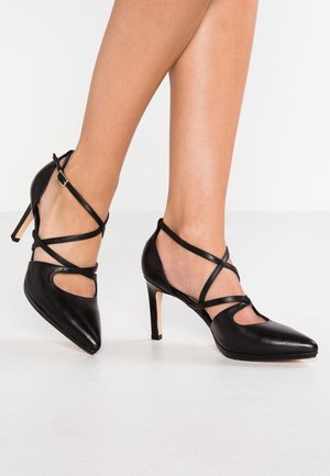 Black leather high heels with pointed toes, crisscross ankle straps, and cut-out details near the arch. Stiletto heels for added height.