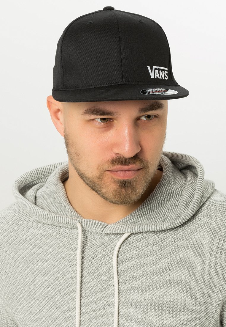 Black snapback cap with white "VANS" logo, flat brim, structured design, made of smooth fabric. Worn with a light grey textured hoodie.