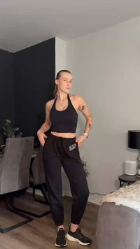 Top cropped preto com alças emparelhado com calças de moletom GAP pretas. A modelo usa ténis pretos, exibindo um estilo athleisure simples e casual.