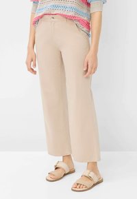 Pantaloni ampi beige chiaro realizzati in tessuto morbido, con tasche frontali e chiusura con un unico bottone. Abbinati a sandali piatti beige.