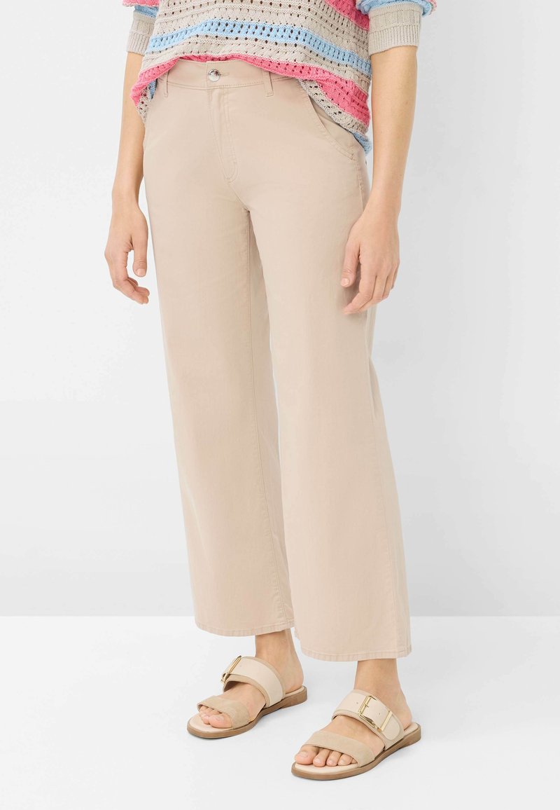 Pantaloni ampi beige chiaro realizzati in tessuto morbido, con tasche frontali e chiusura con un unico bottone. Abbinati a sandali piatti beige.