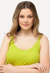 Top de tirantes acanalado de color verde lima con tirantes anchos y escote en V. El material parece suave y elástico, ajustándose al cuerpo.