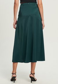 Grüne Satin-Midikleid mit glatter Textur, A-Linie-Silhouette und Reißverschluss hinten, kombiniert mit schwarzen High Heels.