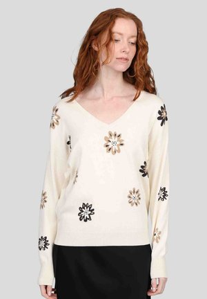 Pull crème avec un col en V et une coupe décontractée, agrémenté de broderies florales noires et beiges. Matière douce et poignets côtelés.
