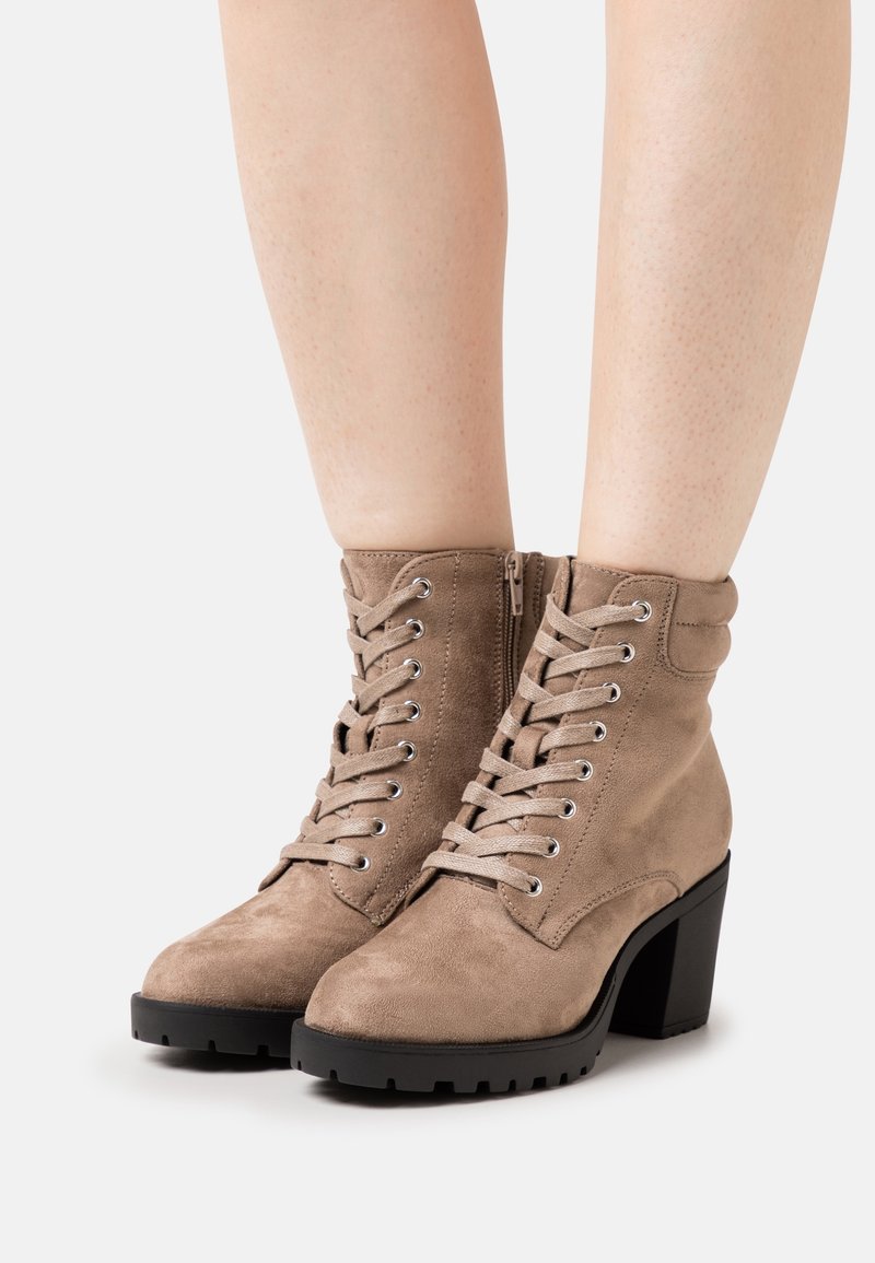 Botines beige de ante con punta redonda, cordones en la parte delantera y cremallera lateral. Presentan un tacón grueso negro y suela texturizada para mayor agarre.