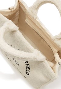 Crèmekleurige fuzzy handtas met een gestructureerde buitenkant, pluche handgrepen en een beige gevoerd interieur met een ritsvak.