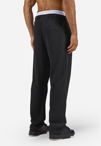 Sorte ribbede sweatpants med en elastisk hvid talje, der har en baglomme, tekstureret stof og en løs pasform.