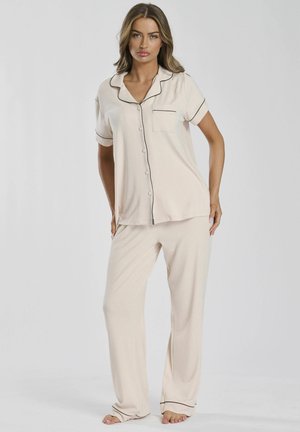 Pajama set in light beige, featuring a short-sleeve top with a button-down front, pocket, and contrasting black piping. Loose-fitting pants.