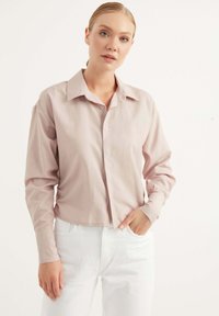 Camicia button-up a maniche lunghe di colore rosa chiaro, con colletto, caratterizzata da una vestibilità comoda e tessuto di cotone liscio. Abbinata a pantaloni bianchi.