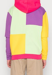 Sudadera colorida con capucha que presenta un diseño de patchwork con secciones en rosa, amarillo, verde y púrpura. Tejido suave y puños acanalados.