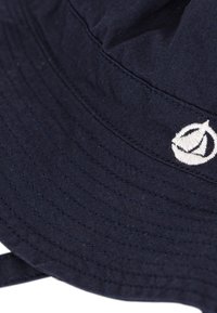 Marineblauwe buckethoed gemaakt van katoen. Heeft een gestikte rand en een wit geborduurd logo. Zachte textuur en een ronde, ontspannen vorm.