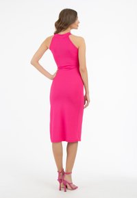 Abito midi aderente in vivace materiale a coste rosa, con colletto alto e design con schiena scoperta, abbinato a tacchi rosa con cinturini.