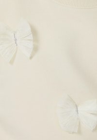 Maglione crema chiaro con finitura testurizzata, caratterizzato da due fiocchi in tulle bianco trasparente accentuati da un filo d'argento al centro.