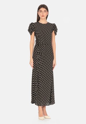 Abito nero a pois con maniche a sbuffo, lunghezza midi, dettaglio arricciato laterale, realizzato in tessuto morbido, abbinato a scarpe di colore chiaro.