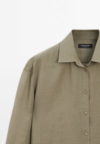 Licht olijfgroen linnen shirt met een puntkraag, knopen aan de voorkant en een ontspannen pasvorm. Bevat subtiele textuur en een minimalistisch ontwerp.