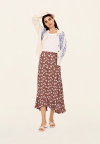Kevyt kerrosmekko, jossa on sinisiä kukkakoristeita, valkoinen pusero ja ruskea kukkakuviollinen maksimekko, jossa on röyhelöhelma. Beige kankaiset korkokengät.