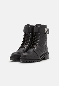 Botas de tobillo de cuero negro acolchado con punta redonda, diseño de cordones, suela de goma contrastante y una correa decorativa con un acento circular.