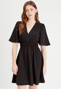 Abito nero con scollo a V, maniche corte a campana e vita elasticizzata. Realizzato in tessuto texturizzato con una gonna fluente.