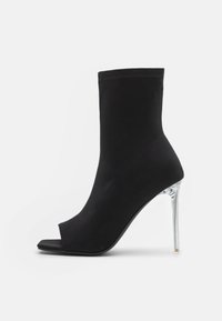 Mustat nilkkurit, jotka on valmistettu sileästä kankaasta, avonaisella varpaalla, tiukalla varrella ja läpinäkyvällä korkolla.