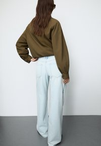 Luźna oliwkowozielona koszula z długimi rękawami, zestawiona z jasnoniebieskimi, szerokimi spodniami z wysokim stanem. Gładka tekstura, minimalistyczny design.