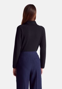 Czarny, dopasowany sweter z golfem i rękawami raglanowymi, w połączeniu z spodniami o wysokim stanie i szerokich nogawkach w kolorze granatowym, z tylnymi kieszeniami.