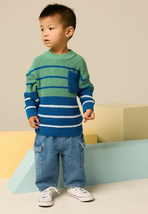 Gestreifter Strickpullover in Grün und Blau mit einer Tasche, kombiniert mit lockeren Jeans-Cargo-Hosen und weißen Sneakers.
