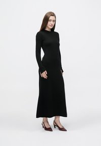 Abito nero a maniche lunghe in tessuto a maglia strutturato, aderente sul corpetto e svasato sull'orlo, abbinato a décolleté color borgogna con punta a mandorla.