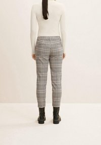 Grå rutiga byxor med slim fit, utrustade med två bakfickor och tillsammans med svarta kängor med tjock sula. Modellen ses bakifrån.