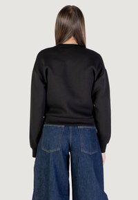 Felpa nera con collo rotondo e spalle scese, abbinata a jeans in denim blu a gamba larga con tasche posteriori.