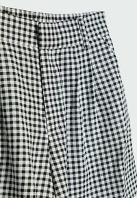 Tela de cuadros vichy en blanco y negro con pliegues, con una cinturilla en la parte superior. La textura parece suave y tejida.