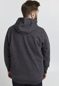Mørk grå hettegenser med en teksturert overflate, justerbar hette og ribbestrikkede mansjetter. Enkelt, avslappet snitt uten synlige logoer eller mønstre.