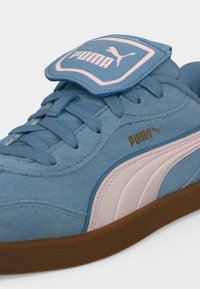 Μπλε σουέντ αθλητικό παπούτσι Puma με ροζ ρίγα, καφέ σόλα, κορδόνια και λογότυπο Puma στη γλώσσα και στην πλευρά.