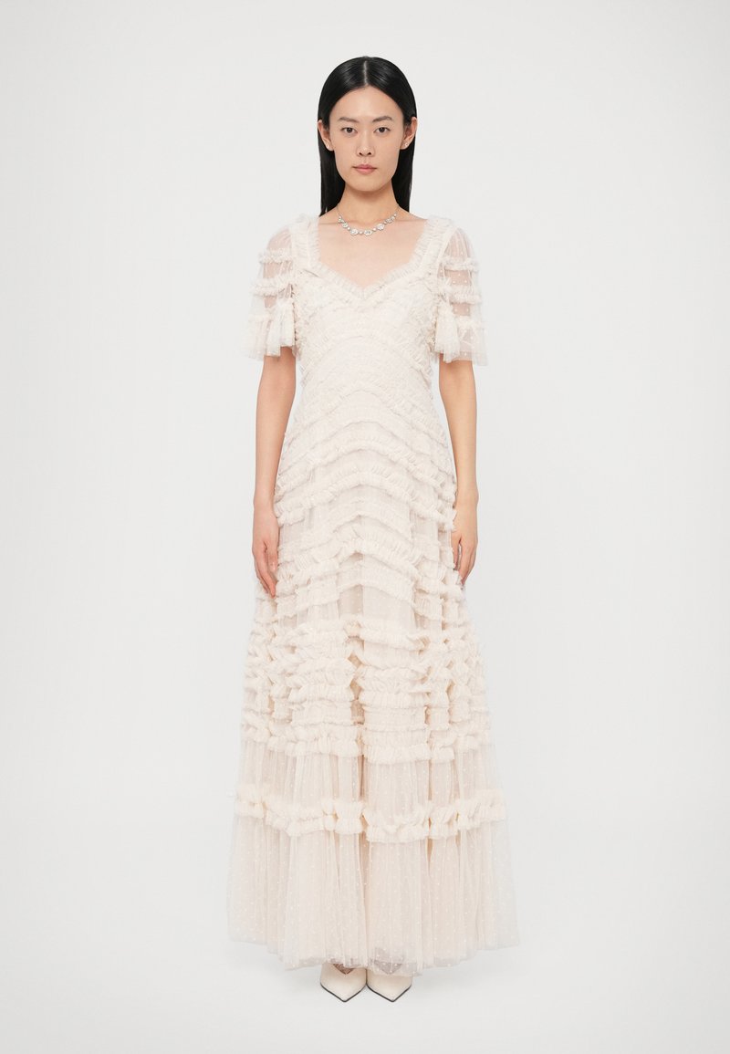 Μακρύ φόρεμα από διάφανο ροζ τούλι, με στρωτές βο�λάν, κοντά φουσκωτά μανίκια και τετράγωνο ντεκολτέ. Το σύνολο ολοκληρώνουν μυτερές γόβες.