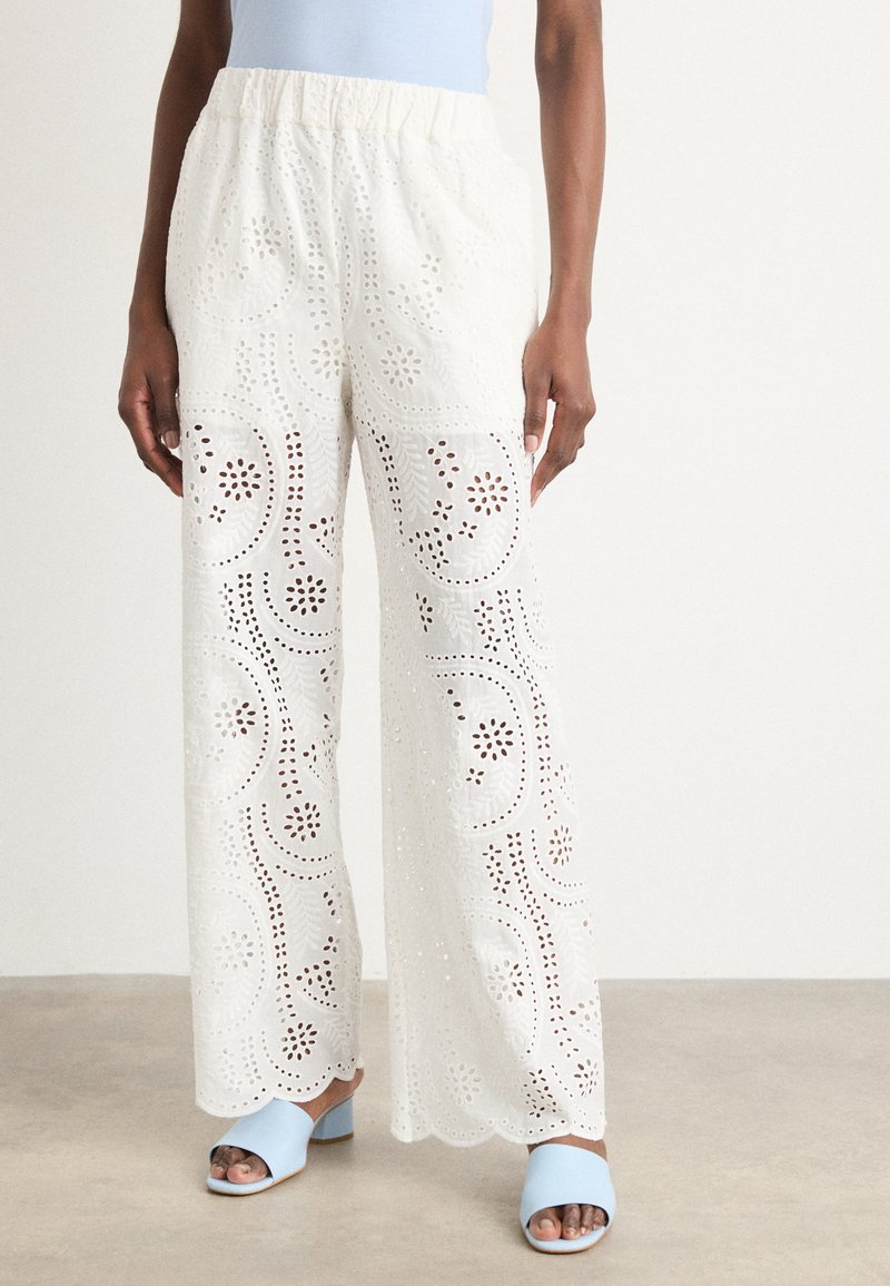 Pantaloni ampi bianchi ricamati presentano motivi floreali a taglio, una vita elastica e orli scallop. Abbinati a tacchi azzurri chiari.