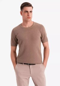 Top de punto beige texturizado de manga corta con un escote redondo. Combinado con pantalones beige claros y un cinturón negro.