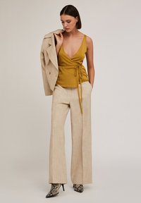 Top dorato con scollo a V profondo e nodo in vita, abbinato a pantaloni beige a gamba larga e tacchi in stampa serpente.
